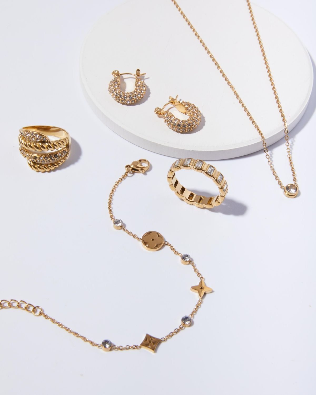 Gouden sieraden op een witte ondergrond, waaronder oorbellen, ringen, een armband en een halsketting.