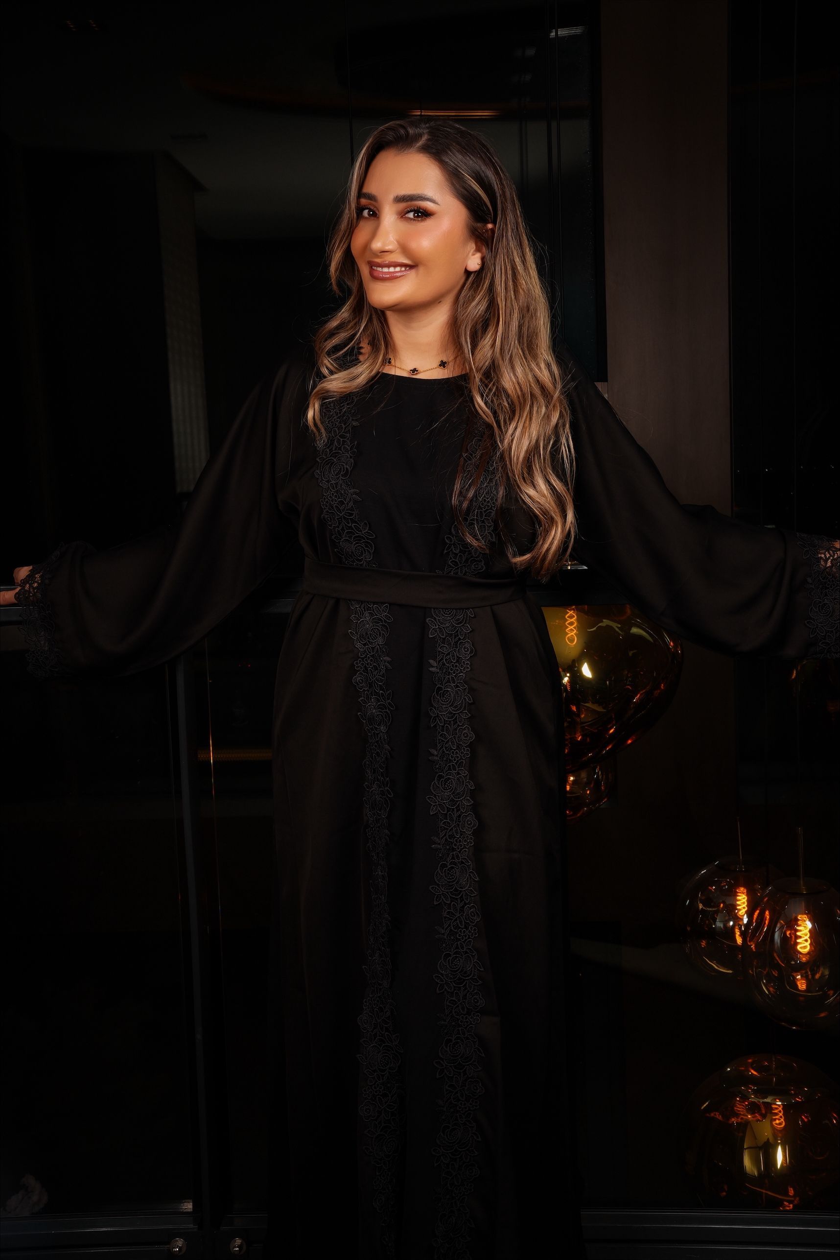 Vrouw in zwarte jurk met kanten details, lachend, binnen.