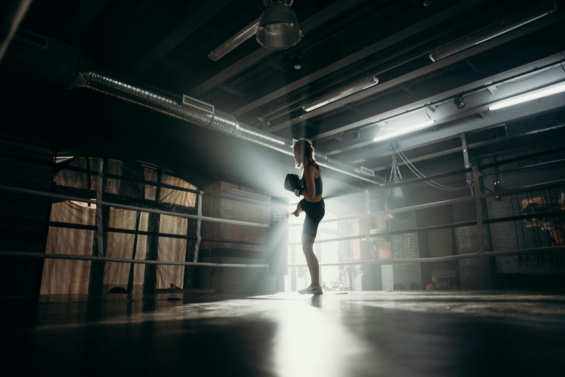 Boxer in a ring, backlit by a beam of light, shadows and a gritty gym setting.