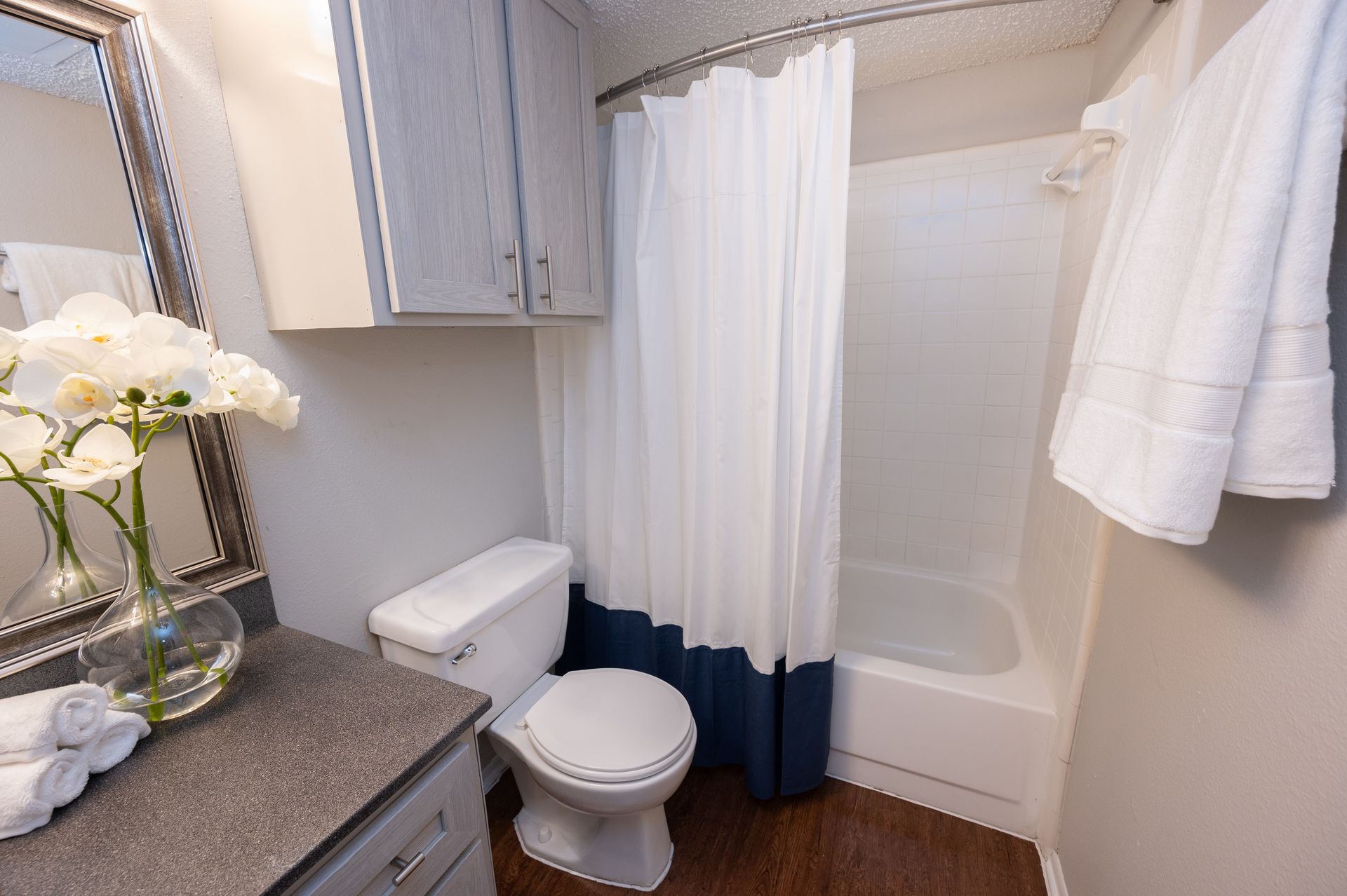 A small bathroom with a toilet, shower/tub, and vanity with flowers. The shower curtain is blue and white.
