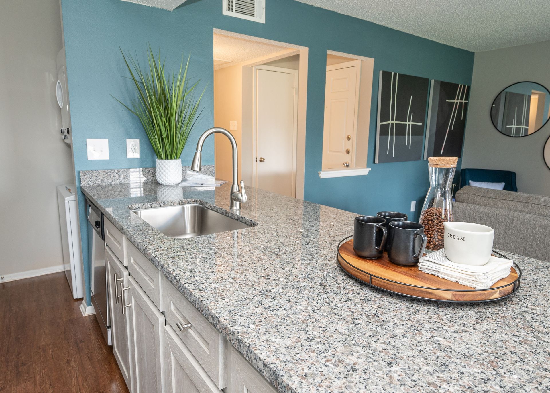 Kitchen with granite countertop, stainless steel sink and faucet, and decorative items on the counter. Turquoise wall in background.