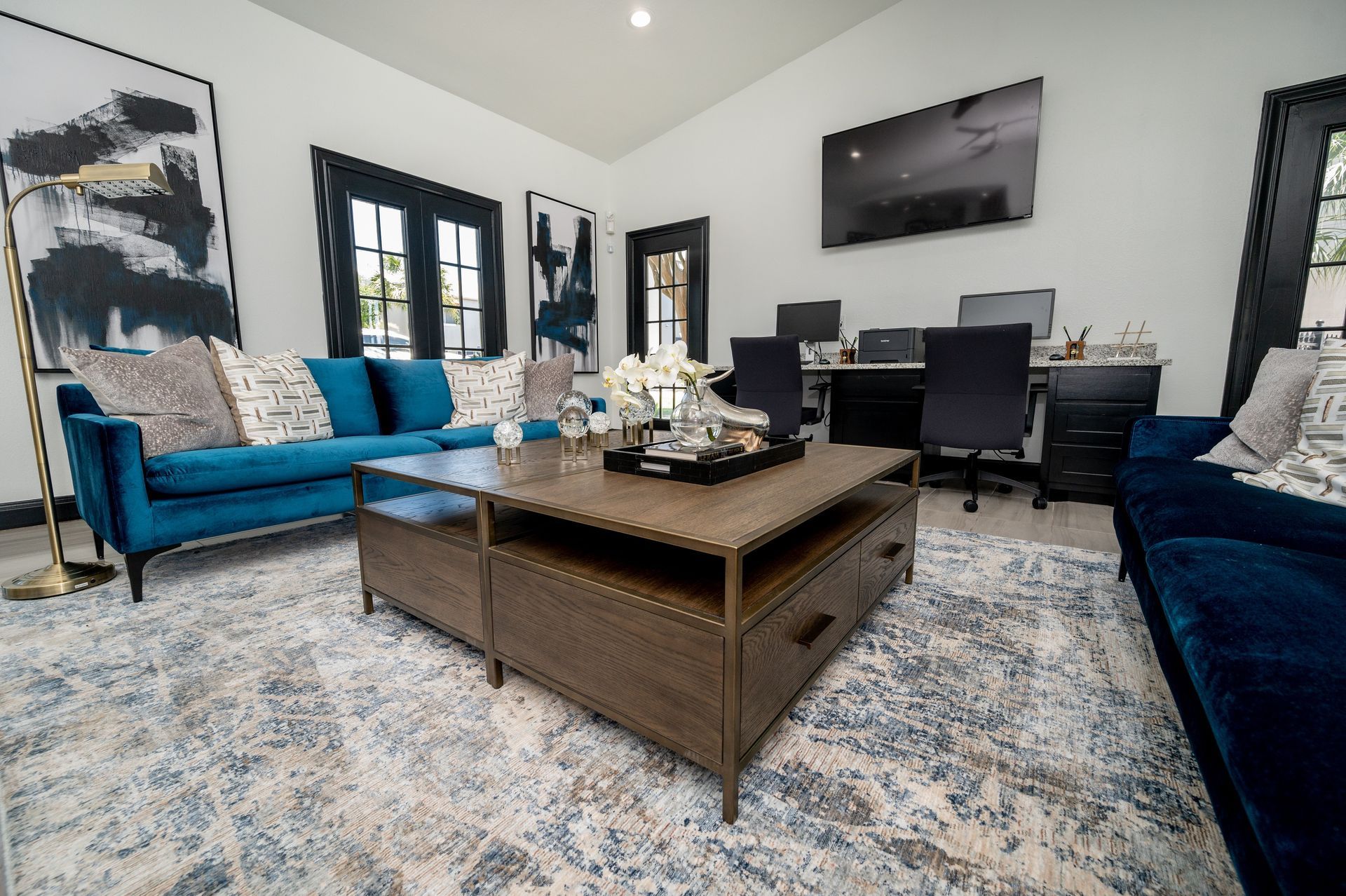 A modern living room with teal couches, a wooden coffee table, and a workspace in the background.