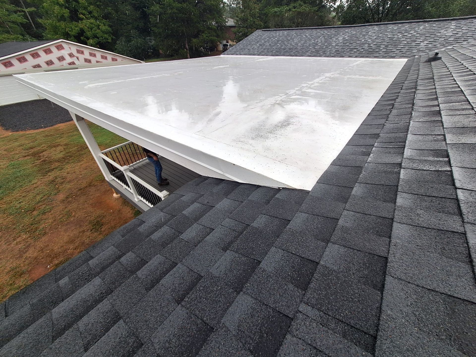 View of a house with a white covered porch, dark gray shingle roof, and green lawn.