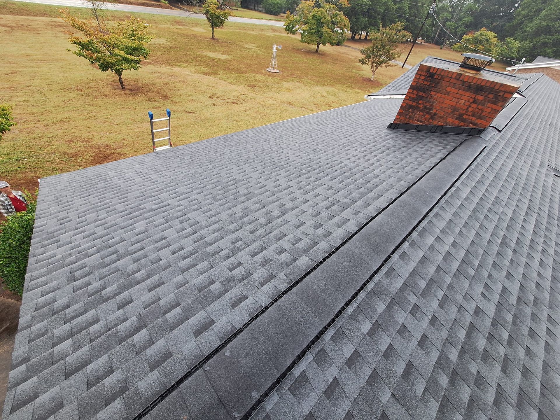 Gray shingle roof with a central black trough. A brick chimney rises.