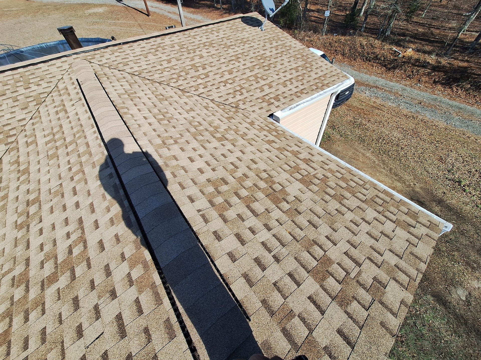 Overhead view of a brown shingled roof with a person's shadow cast across it on a sunny day.