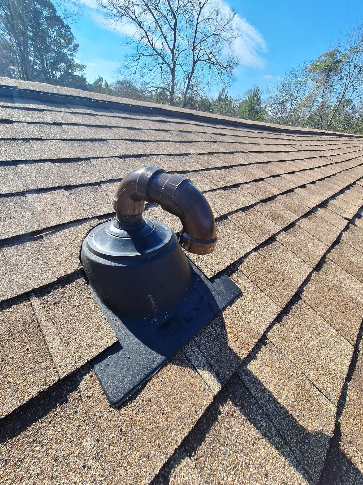 Roof vent with curved pipe on a shingled roof under a blue sky.