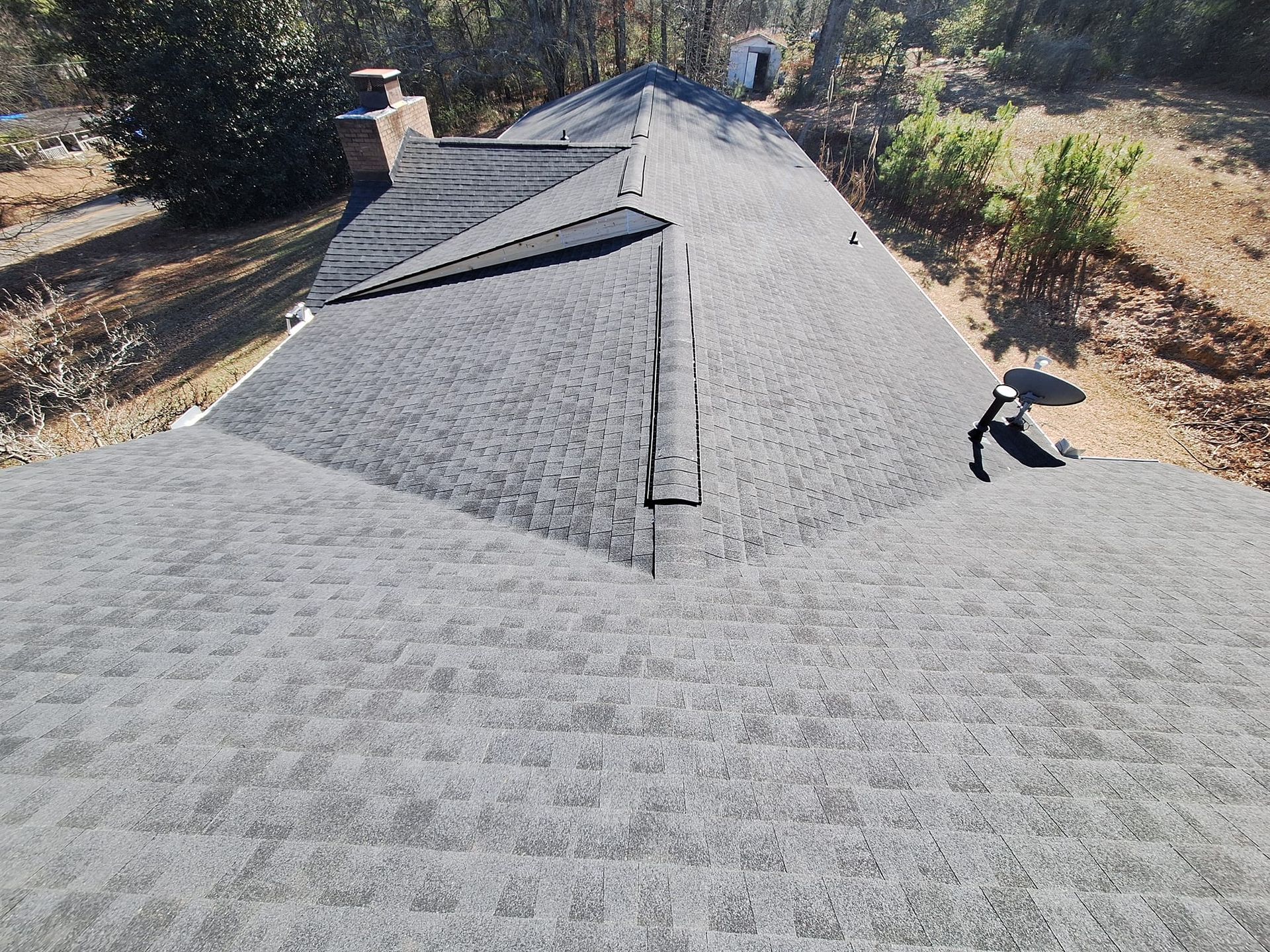Gray shingle roof on a house with a chimney, viewed from above on a sunny day.