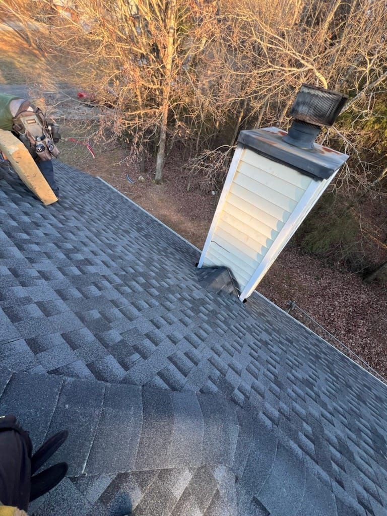 Chimney leaning on a shingled roof; person on the roof holds lumber.