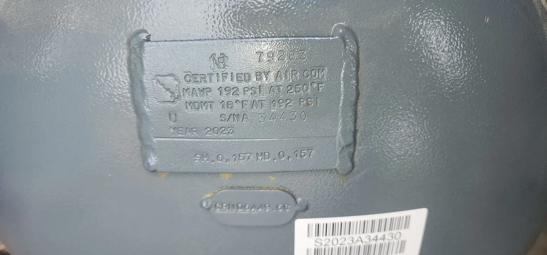 Close-up of a machine part with a metal plate displaying text and numbers. Grey color with a white label at the bottom.