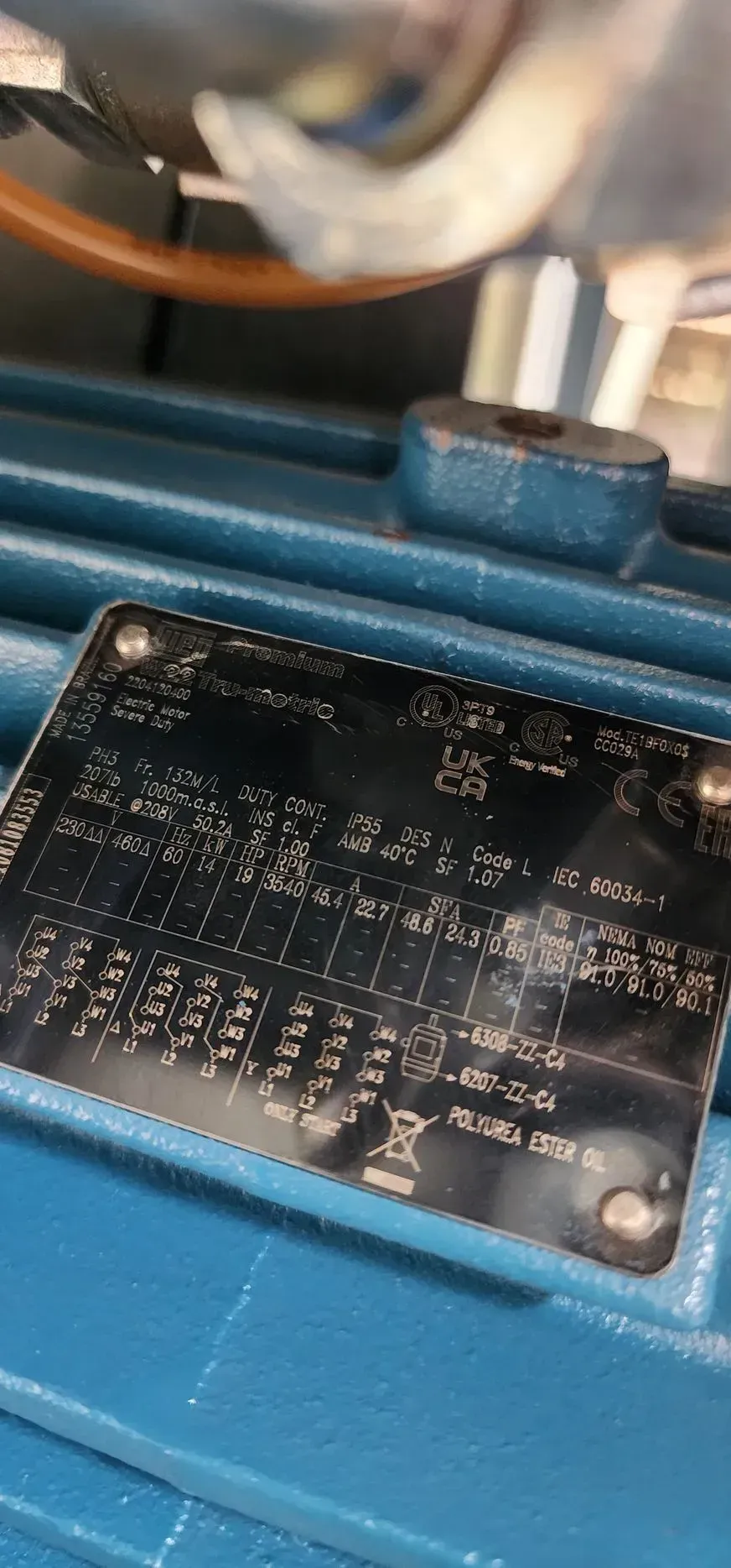 A close-up of a motor nameplate with specifications, mounted on a teal-colored machine.