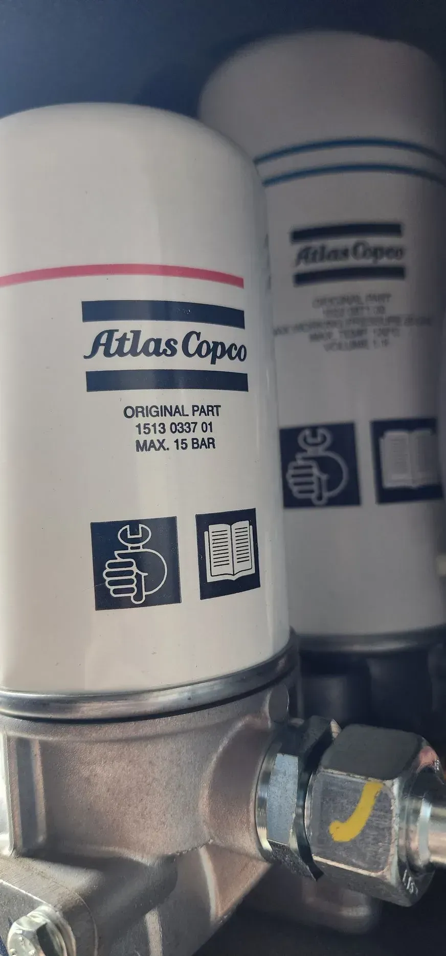 Two Atlas Copco filters, white with red stripe and logos. Attached to a metallic base with tubing.