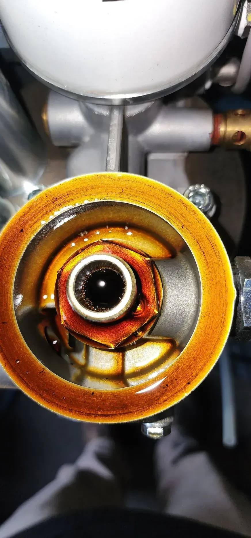 Close-up of a machine component, a ring of brown oil surrounds a central bolt.