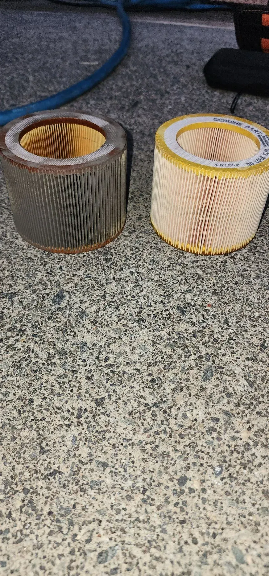 Two cylindrical air filters on a speckled surface; one dirty, the other clean, showing replacement comparison.