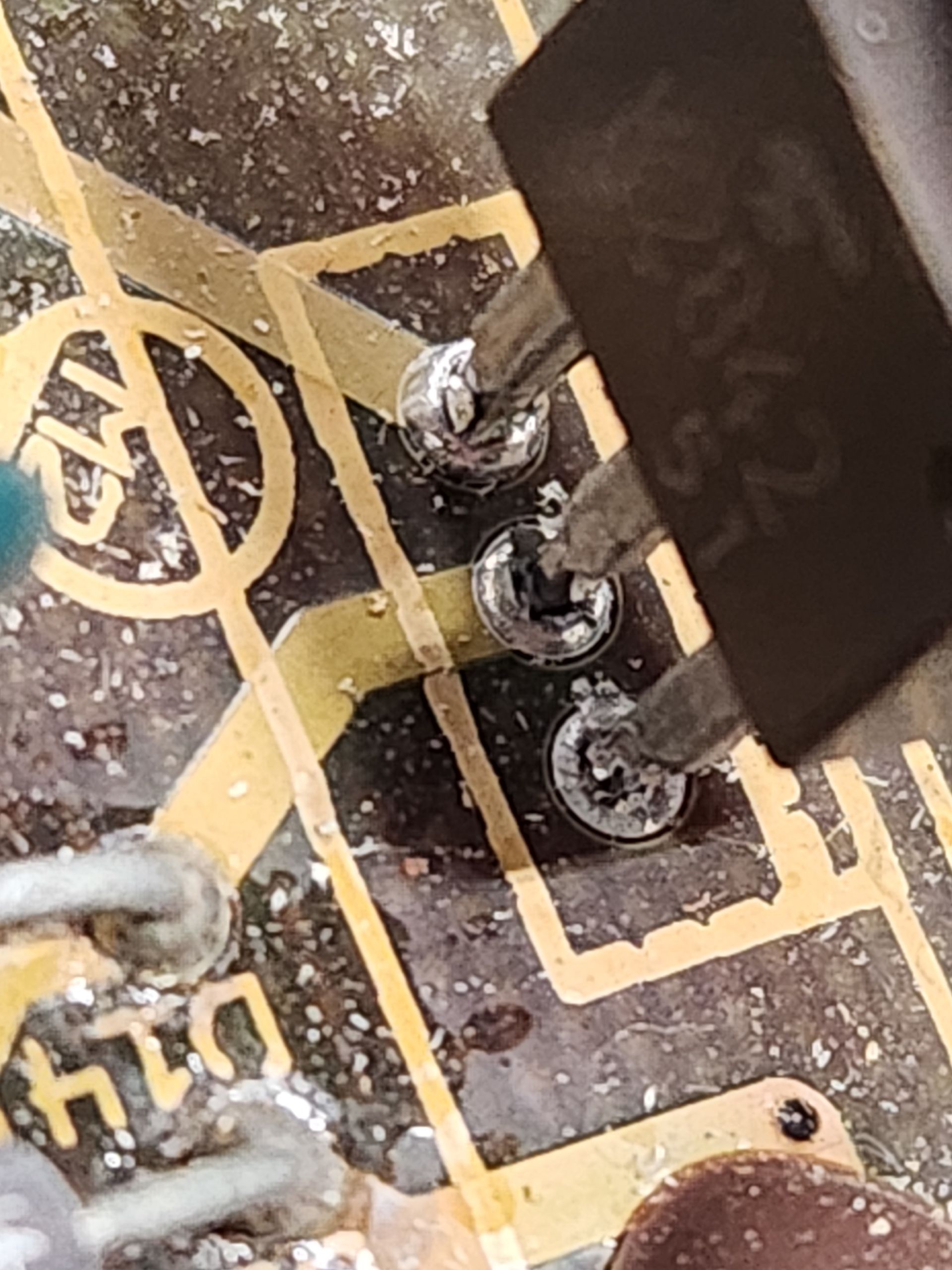 Soldering iron touching three solder joints on a circuit board, near a black component.