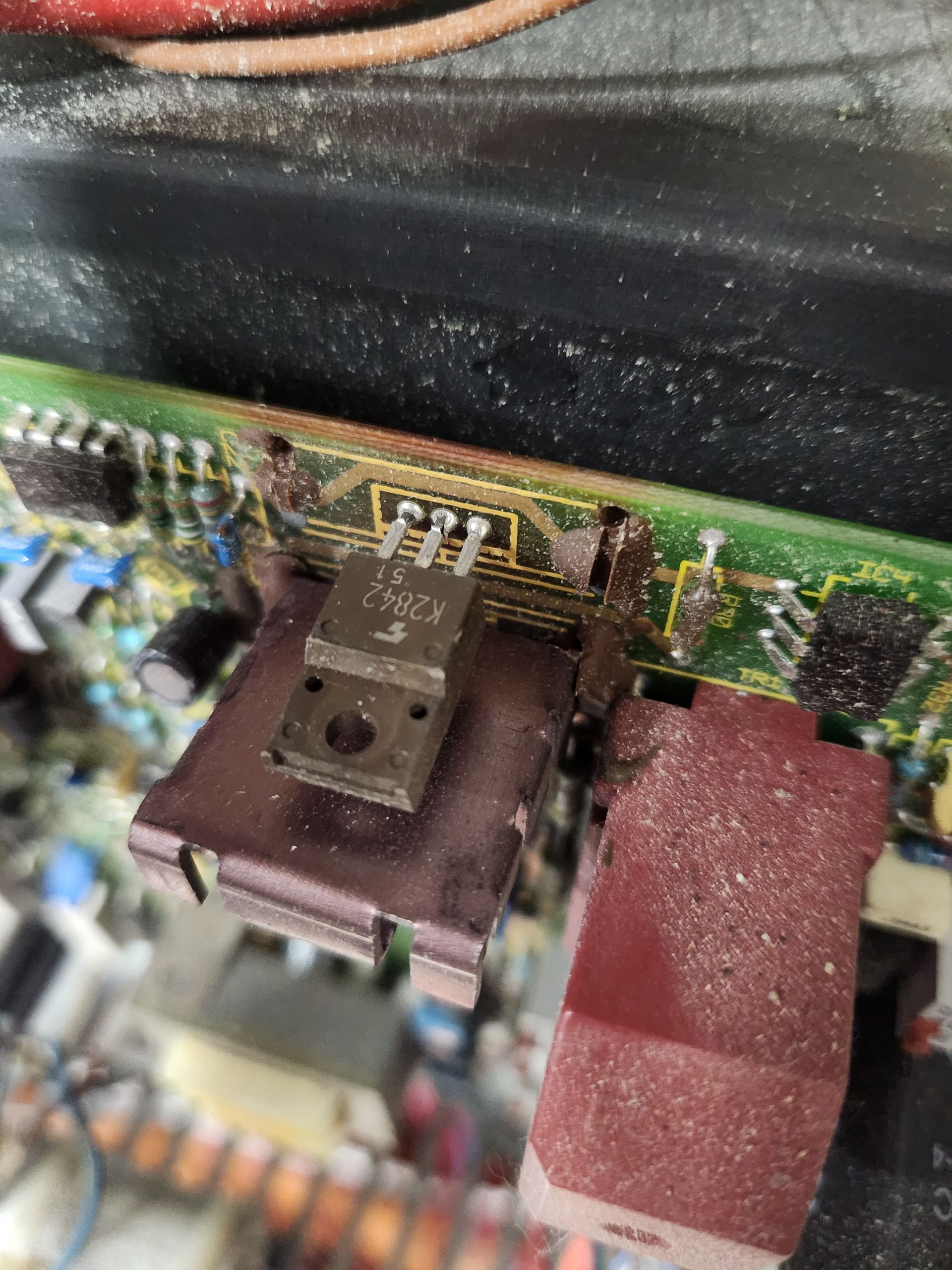 Circuit board with a transistor, a red connector, and dust accumulation.