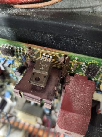 Circuit board with a transistor, a red connector, and dust accumulation.
