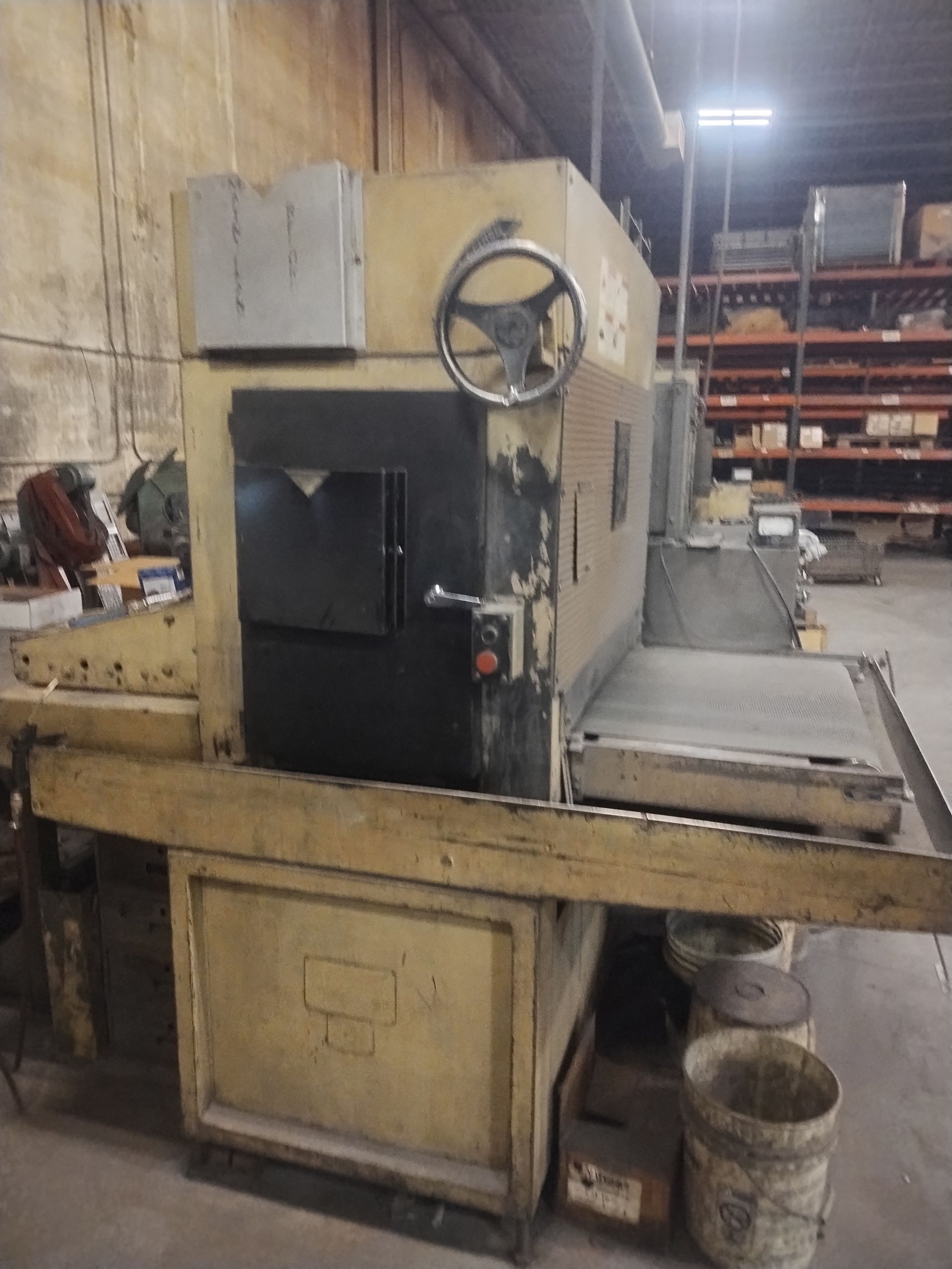 Yellow industrial planer machine in a factory setting, with a black door and hand wheel.