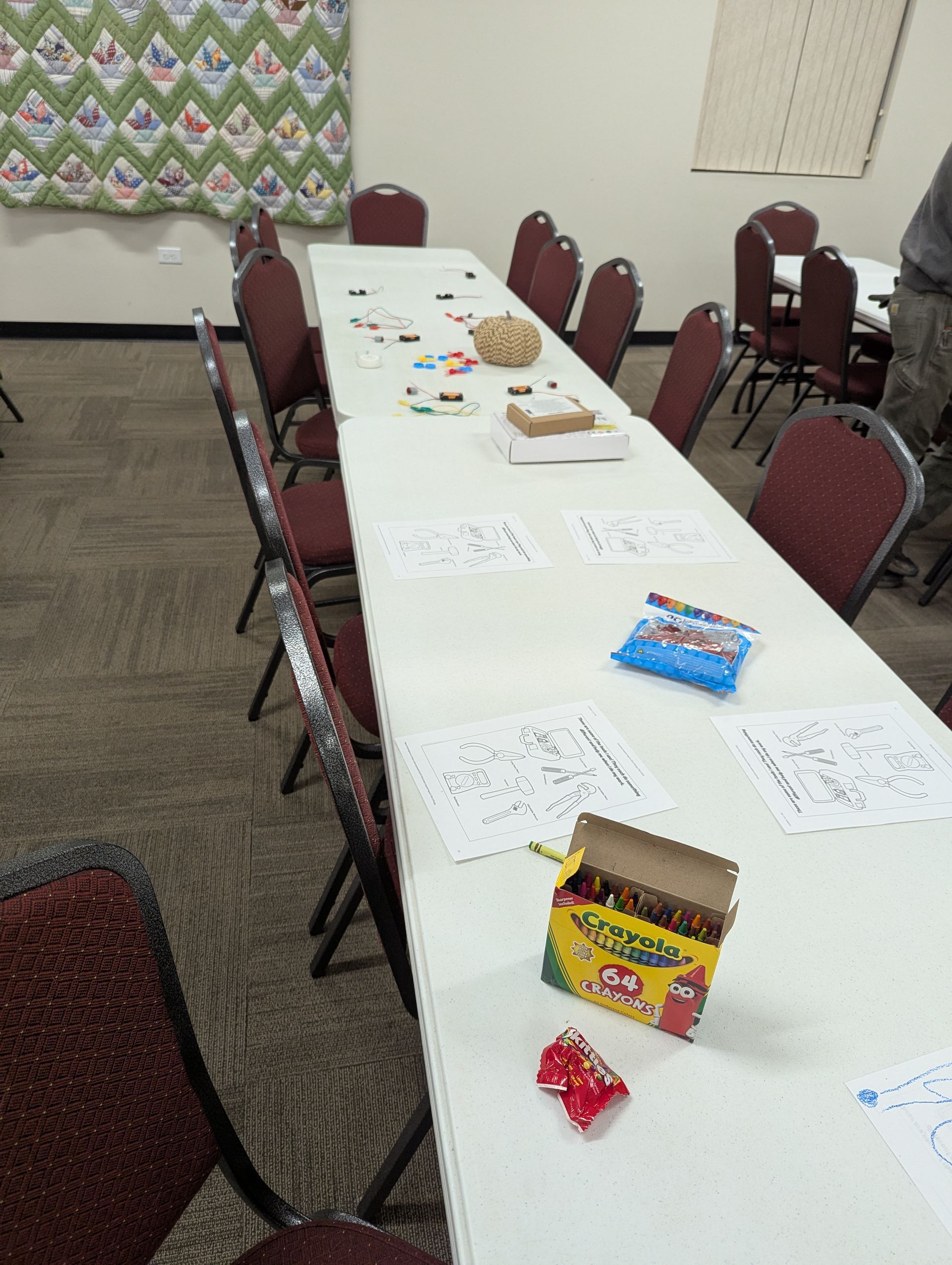 Long rectangular table with chairs. Crayons, coloring pages, and other items on the table.