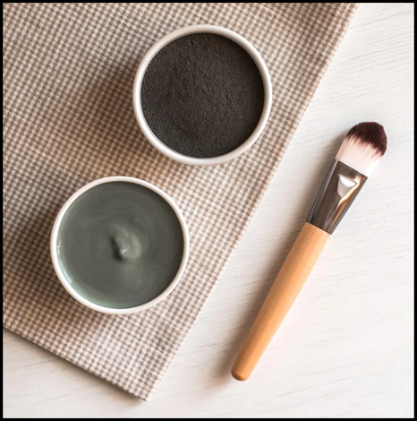 Two small cosmetic bowls and a makeup brush on a beige cloth, overhead view.