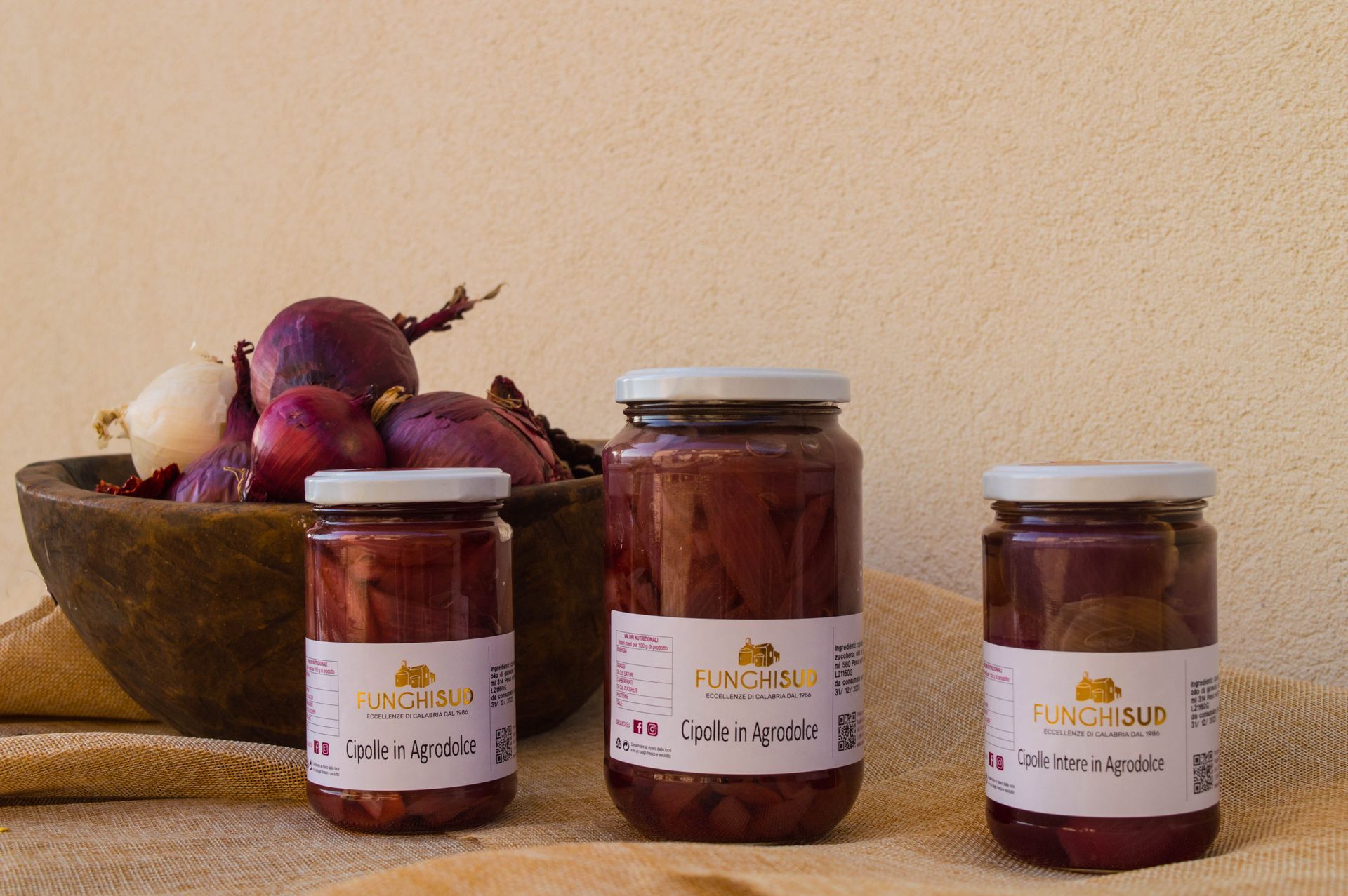 Tre barattoli di cipolle sottaceto sono accanto a una ciotola di cipolle.