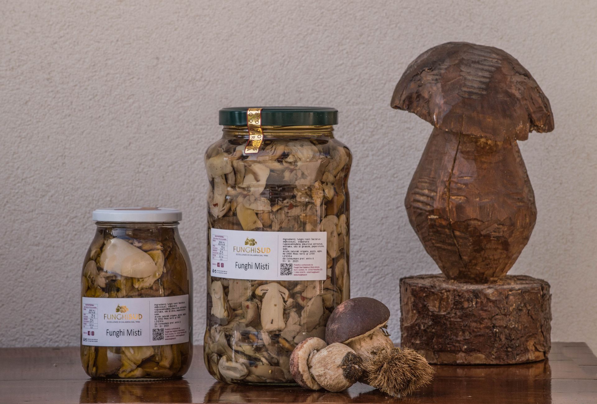 Tre barattoli di funghi sono appoggiati su un tavolo di legno accanto alla statua di un fungo.