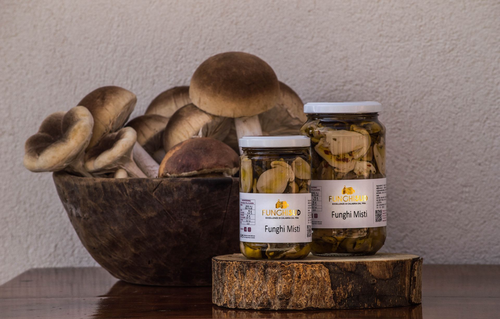 Due barattoli di funghi sono appoggiati su un tavolo di legno accanto a una ciotola di funghi.