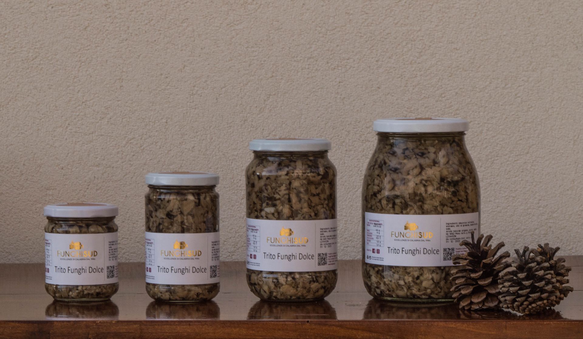 Quattro barattoli di senape sono allineati su un tavolo accanto a delle pigne.