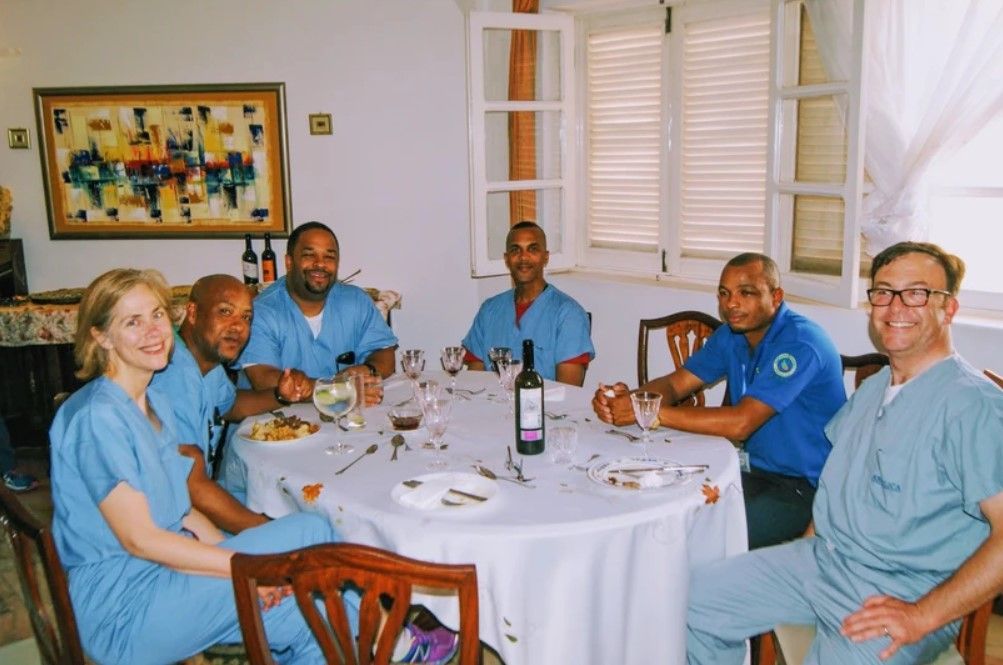 A group of people are sitting around a table with a bottle of wine on it