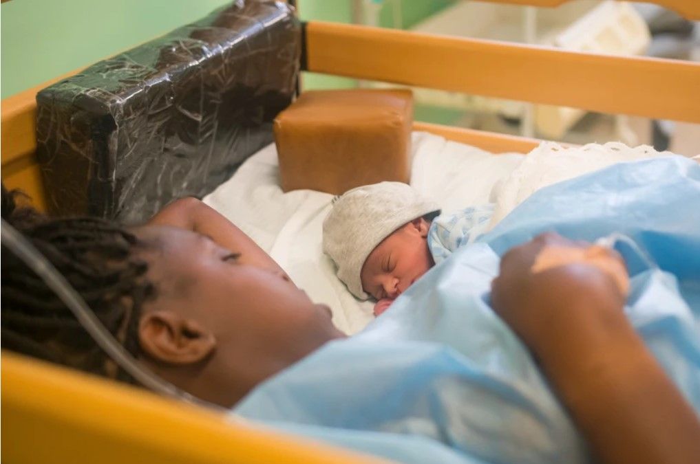 A woman is laying in a hospital bed with a newborn baby.