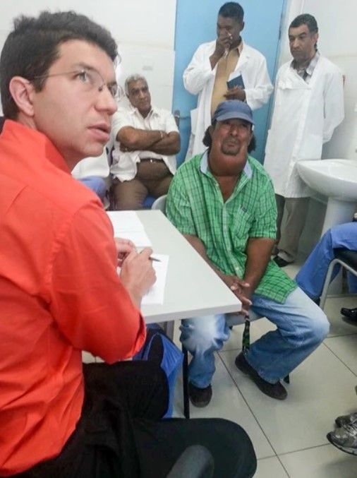 A man in an orange shirt sits at a table with other men