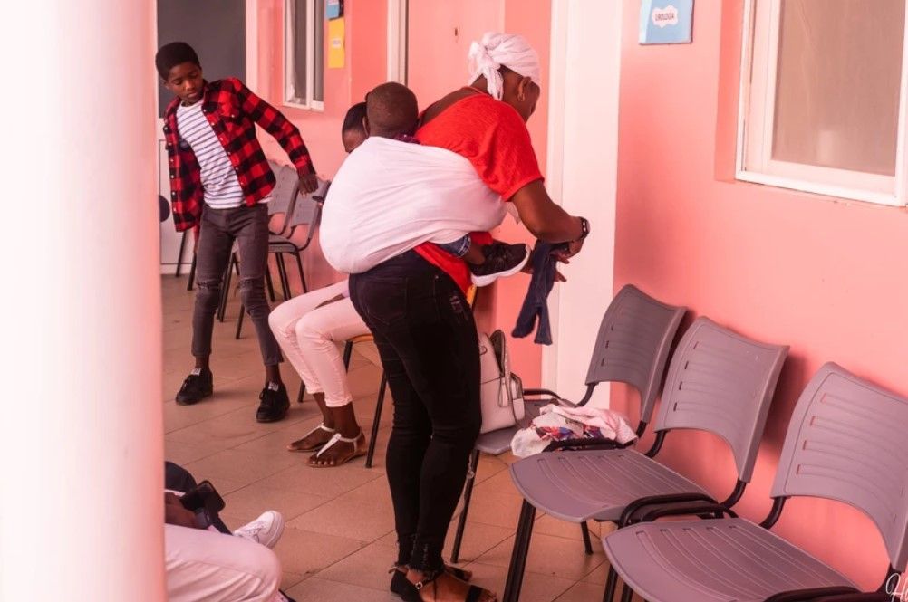 A woman is carrying a child on her back in a waiting room.
