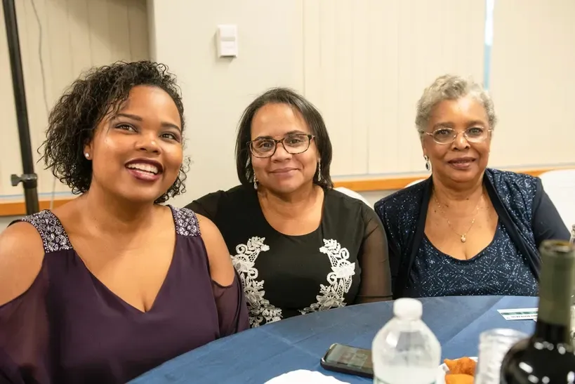 Three women are posing for a picture while sitting at a table.
