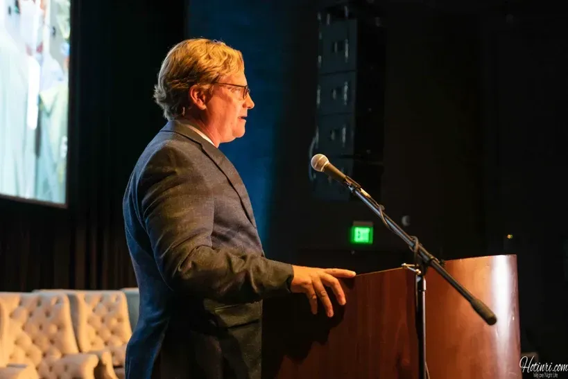 A man in a suit is standing at a podium speaking into a microphone.