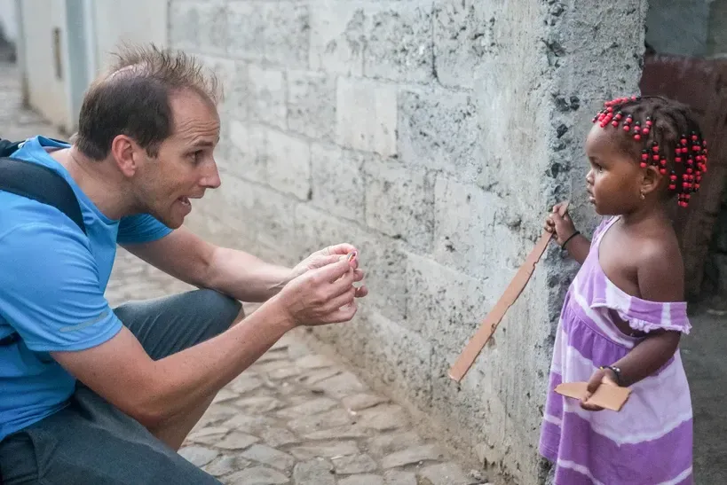 A man is kneeling down next to a little girl in a purple dress.