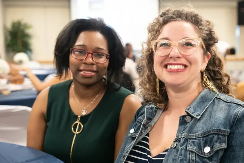 Two women are sitting next to each other and smiling for the camera.