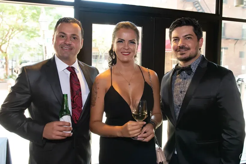 A man in a suit and tie is standing next to a woman in a black dress holding a glass of wine.