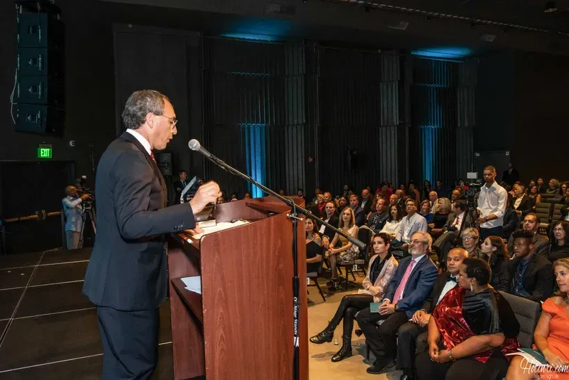 A man is giving a speech at a podium in front of a crowd.