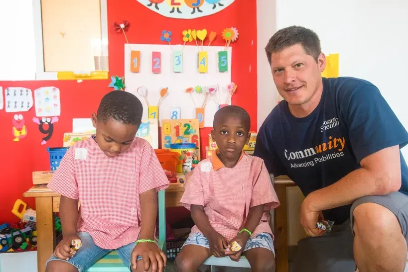 A man is kneeling next to two children in a classroom.