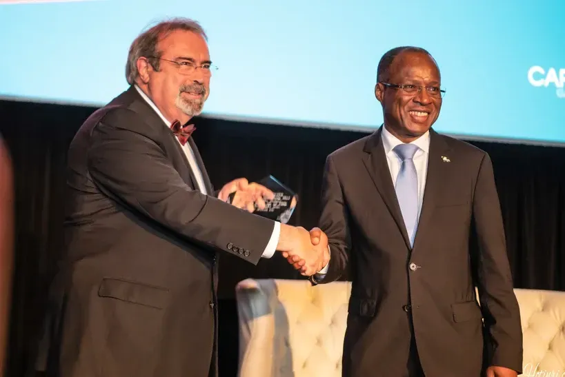 Two men in suits are shaking hands on a stage.