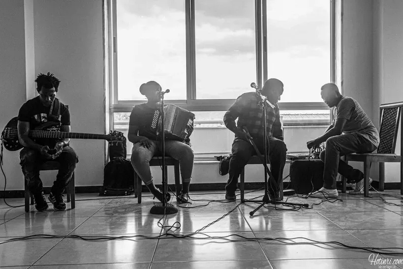 A group of men are playing instruments in a room in front of a window.