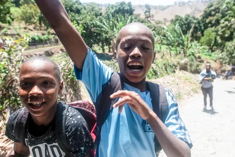 Two young boys are standing next to each other with their arms in the air.