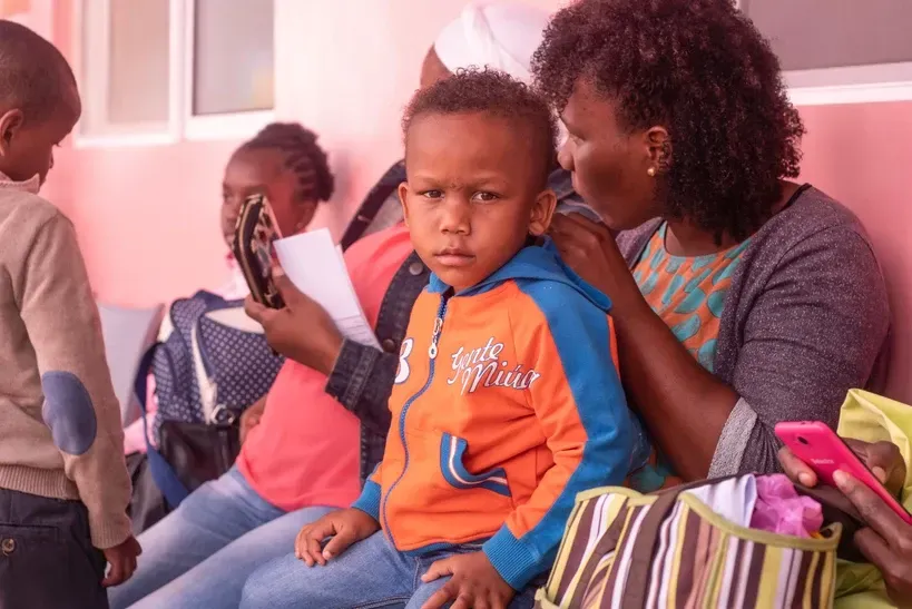A woman is sitting on a bench with a child and holding a cell phone.