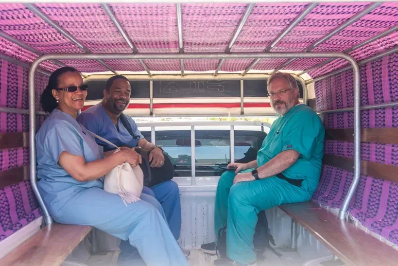 Three people in scrubs are sitting in the back of a truck.