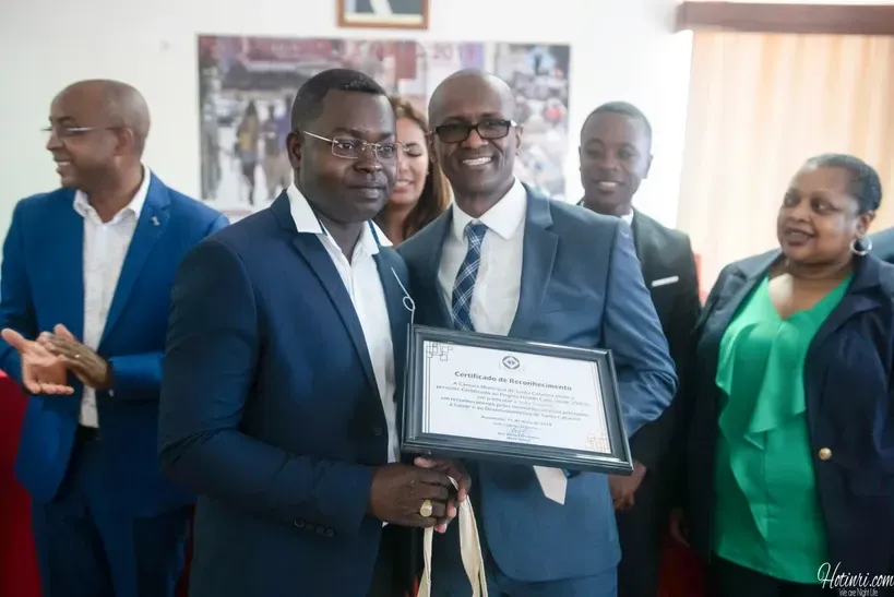 A man in a suit is holding a certificate in front of a group of people.