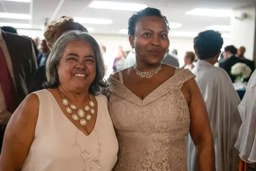 Two women are posing for a picture together in a crowded room.