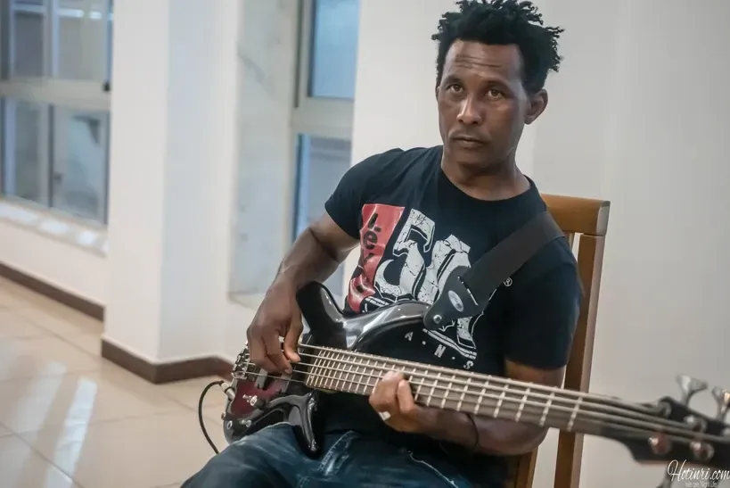 A man is sitting in a chair playing a bass guitar.
