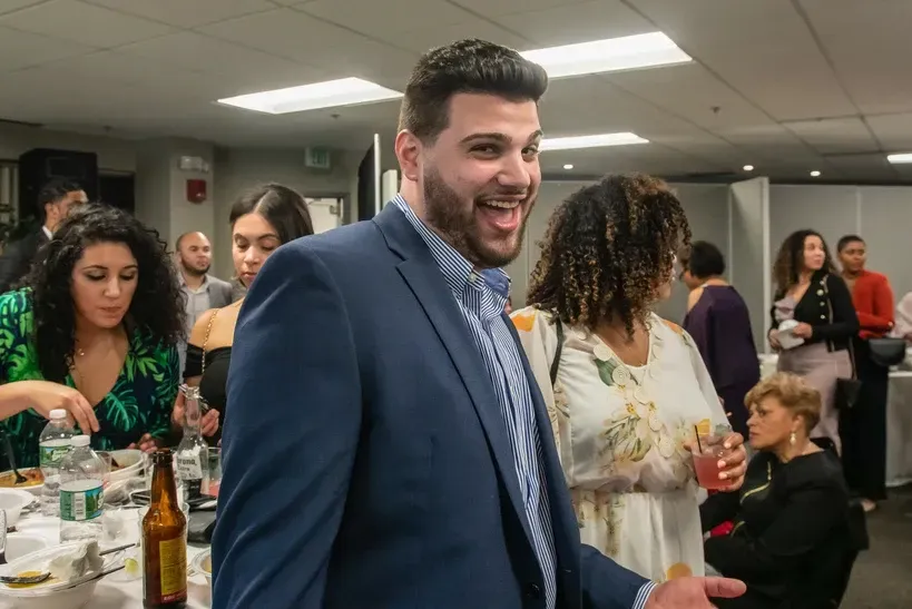 A man in a suit is standing in front of a group of people at a party.