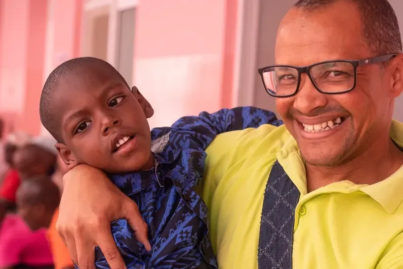 A man wearing glasses is holding a young boy in his arms.