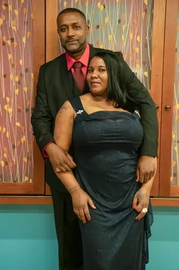 A man in a suit and tie stands next to a woman in a blue dress