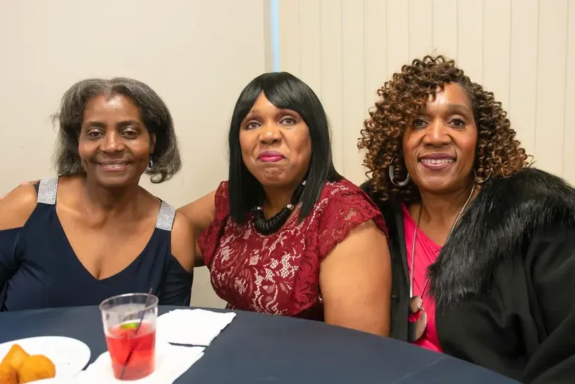 Three women are posing for a picture while sitting at a table.